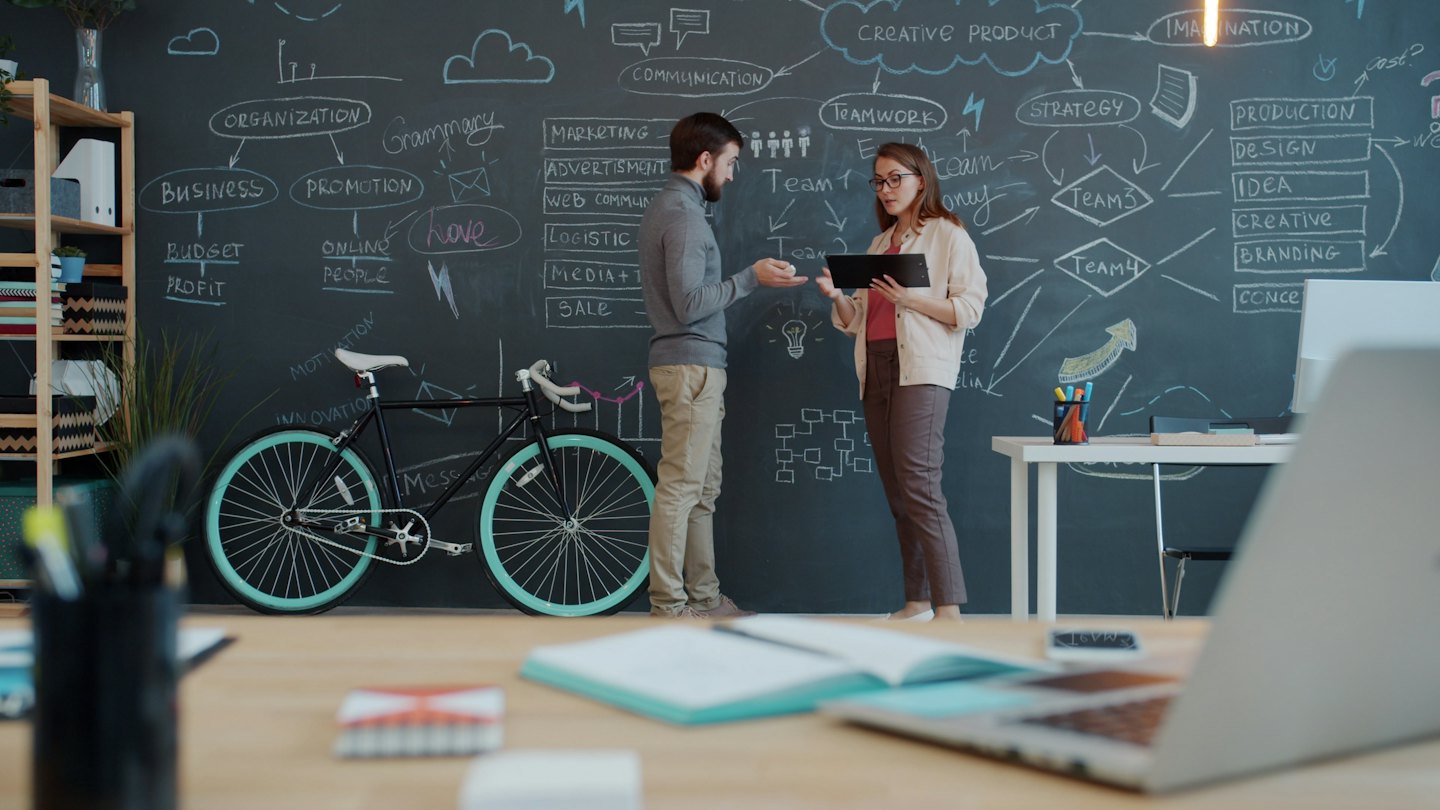 Two professionals discussing a business plan with diagrams on a chalkboard.